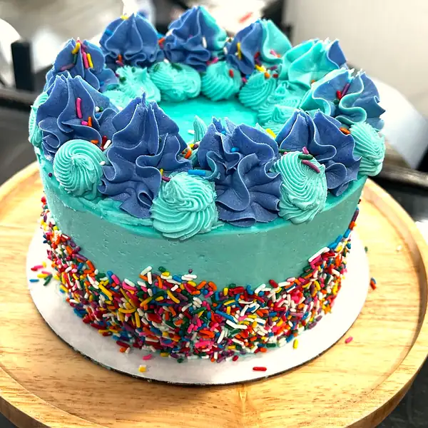 A layer cake frosted in teal with blue rosettes and rainbow sprinkles